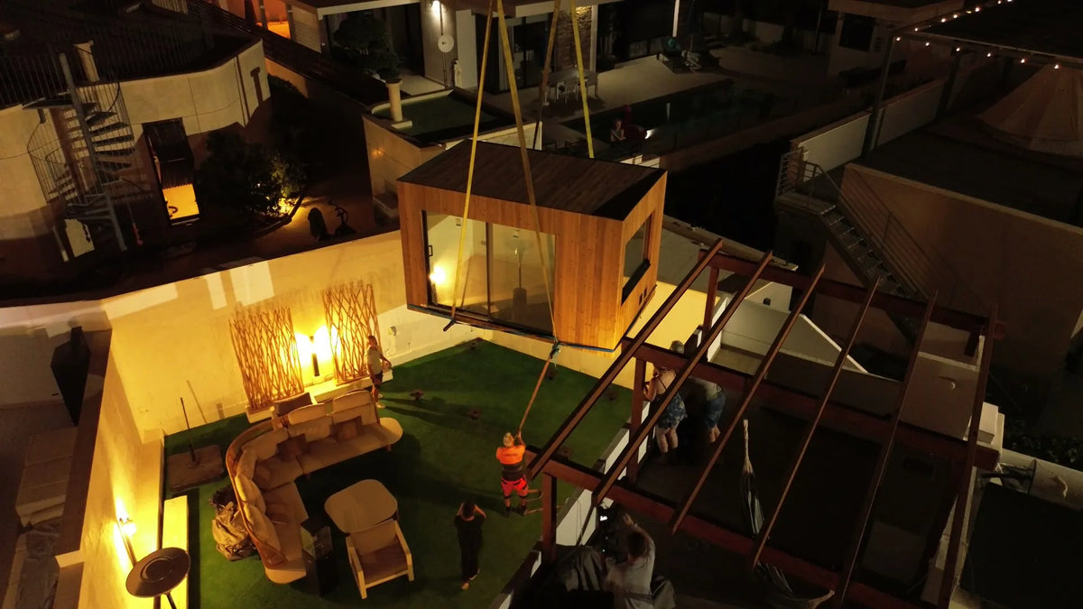 A crane lowers a finished NOOK 10 towards the screw piles of a private garden
